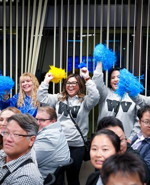 Cheering group of women in gray sweatshirts with yellow and blue pom-poms.