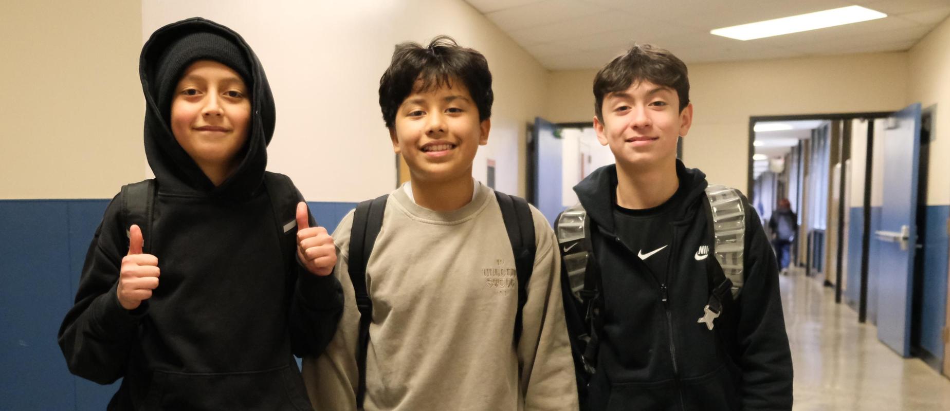 Three boys in a school hallway smiling and posing for the camera.