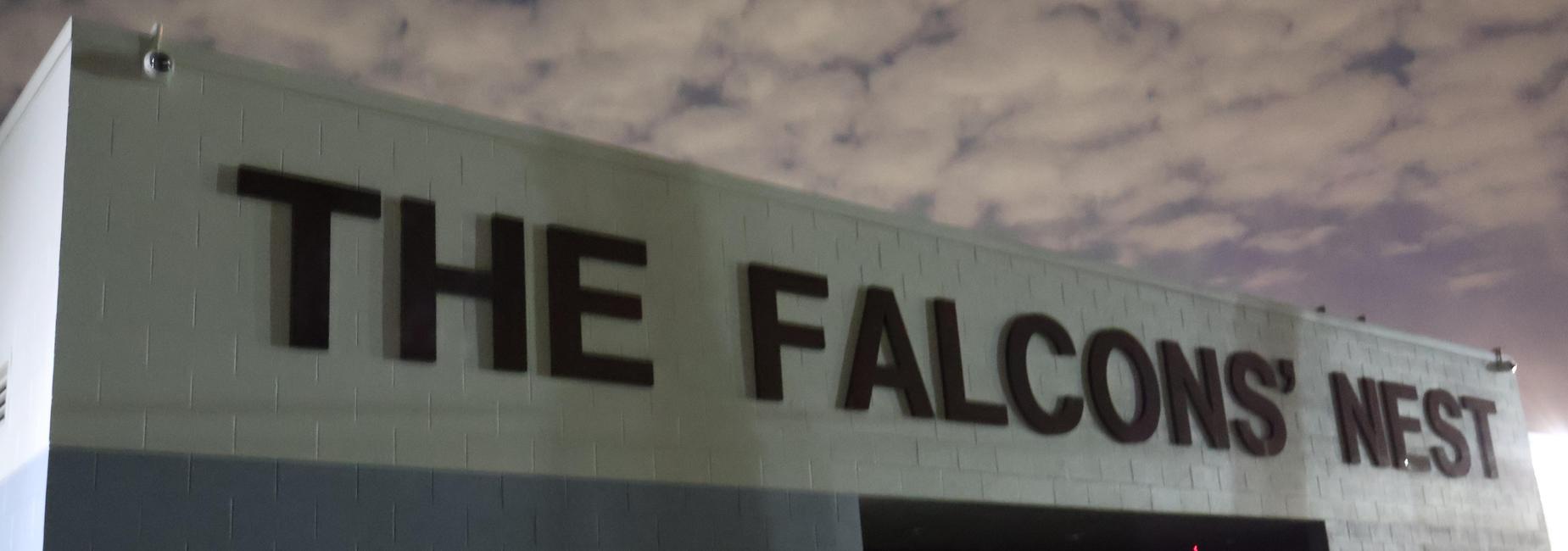 Sign on a building reading 'THE FALCONS' NEST' against a cloudy sky.