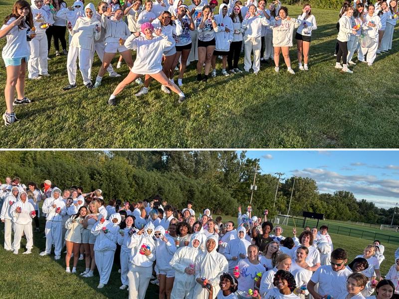 Two large groups of students dressed in white outfits, gathering joyfully on a grassy field.