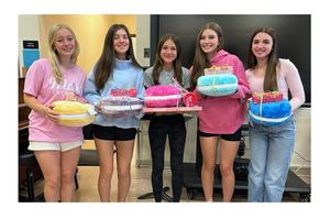 Five high school girls holding pastel colored pillows each with a wrapped present on top