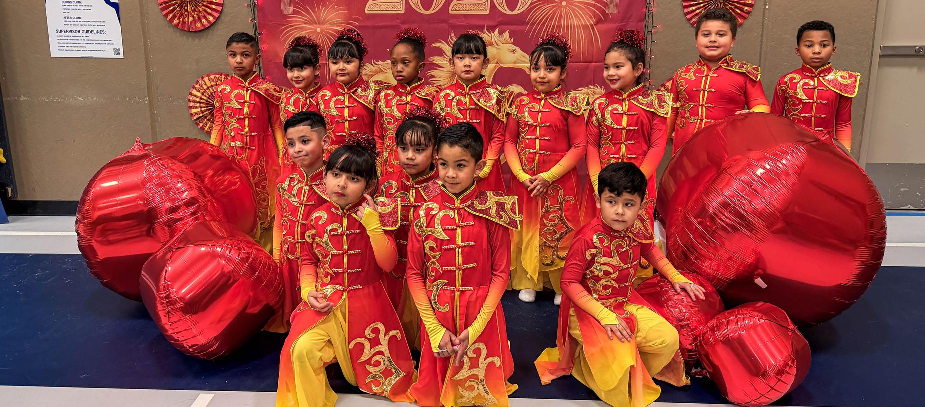 Children in red costumes pose with large red decorations and a festive backdrop.