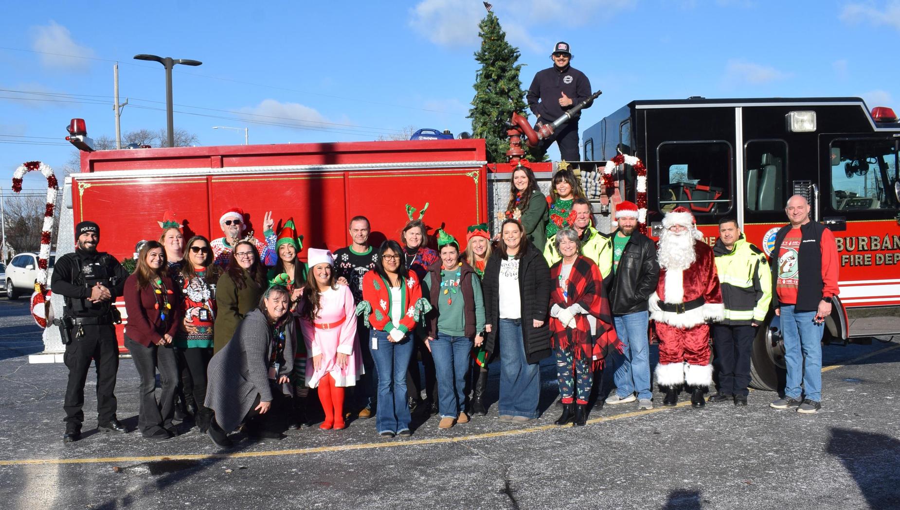A large group posing in festive attire near a fire truck during a holiday celebration.