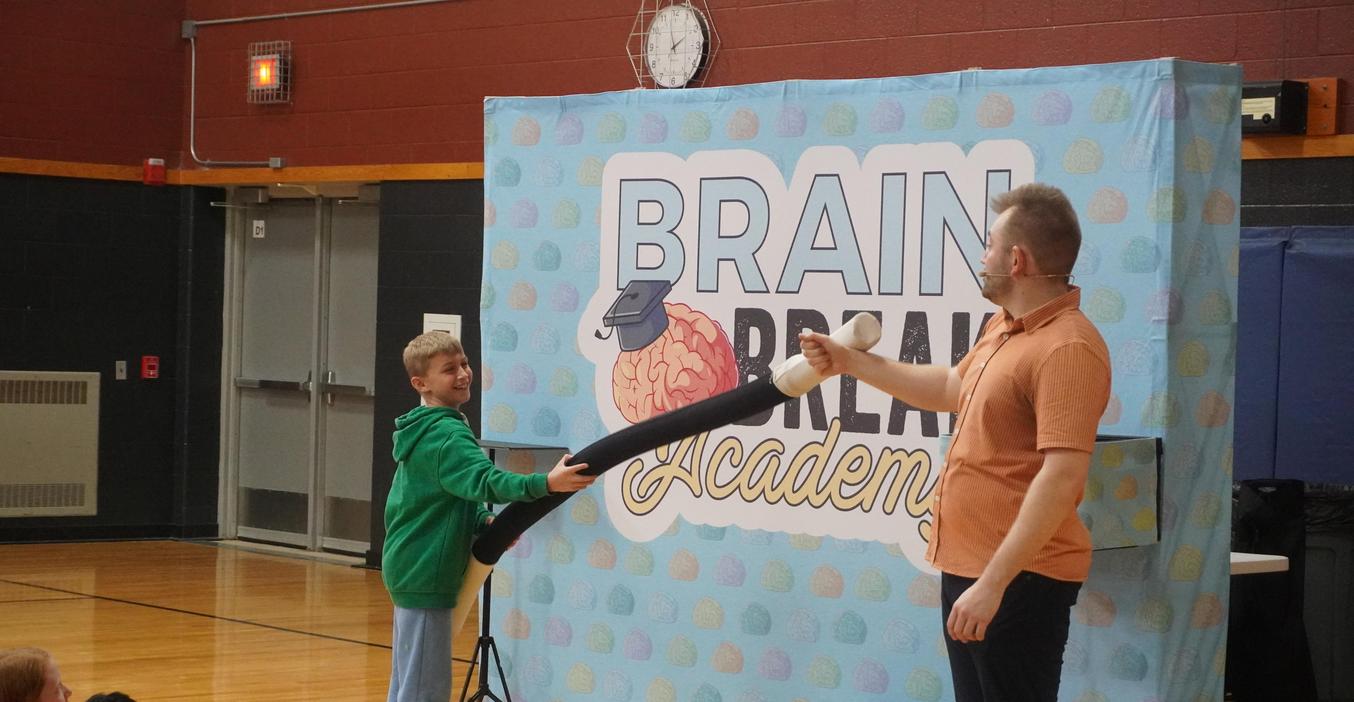 A student uses an extra-long magic wand to help a magician during a Brain Break assembly.
