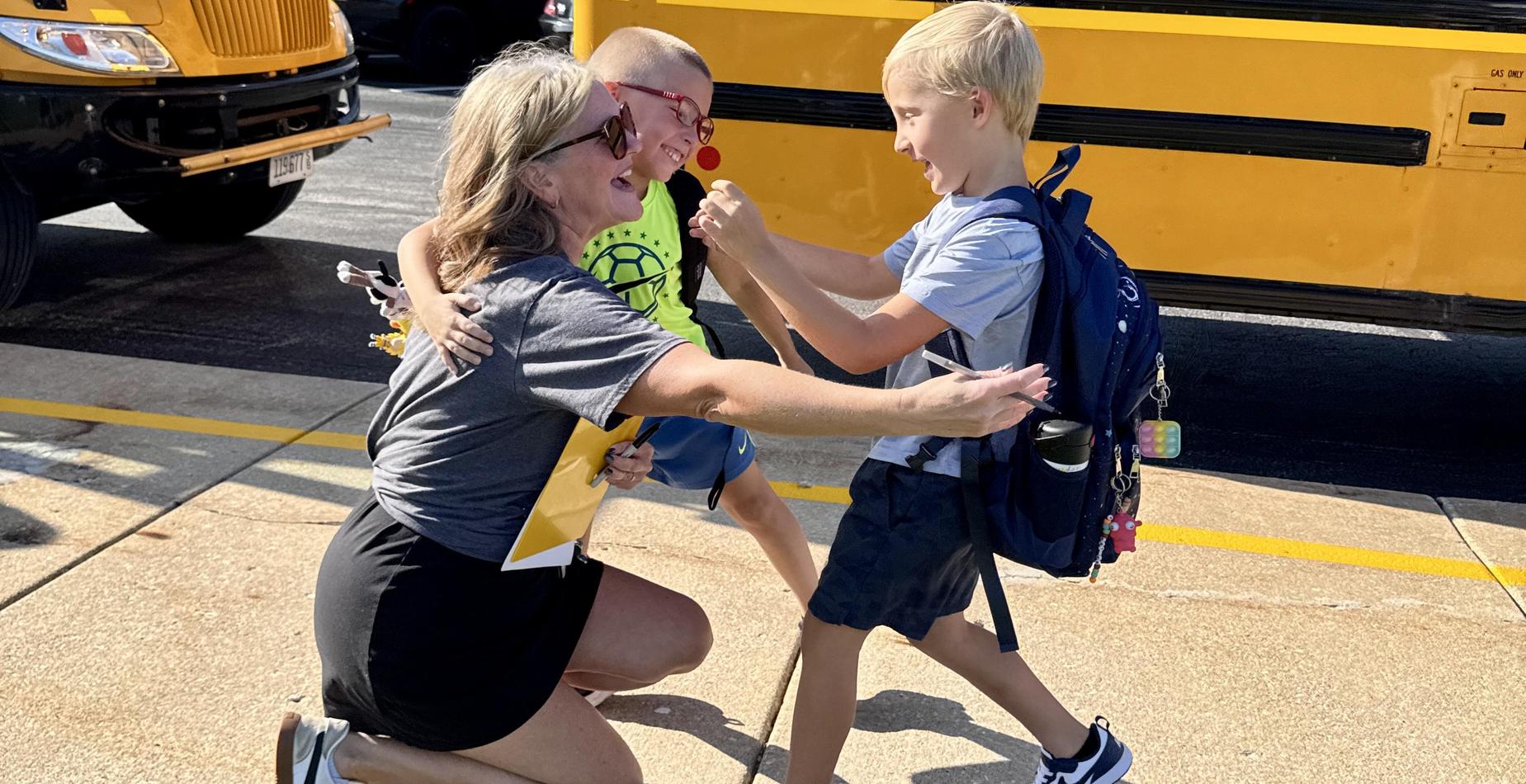 Students greet a teacher with hugs on the first day of school.