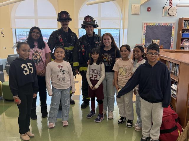 Firefighters pose with a group of children in a library setting.