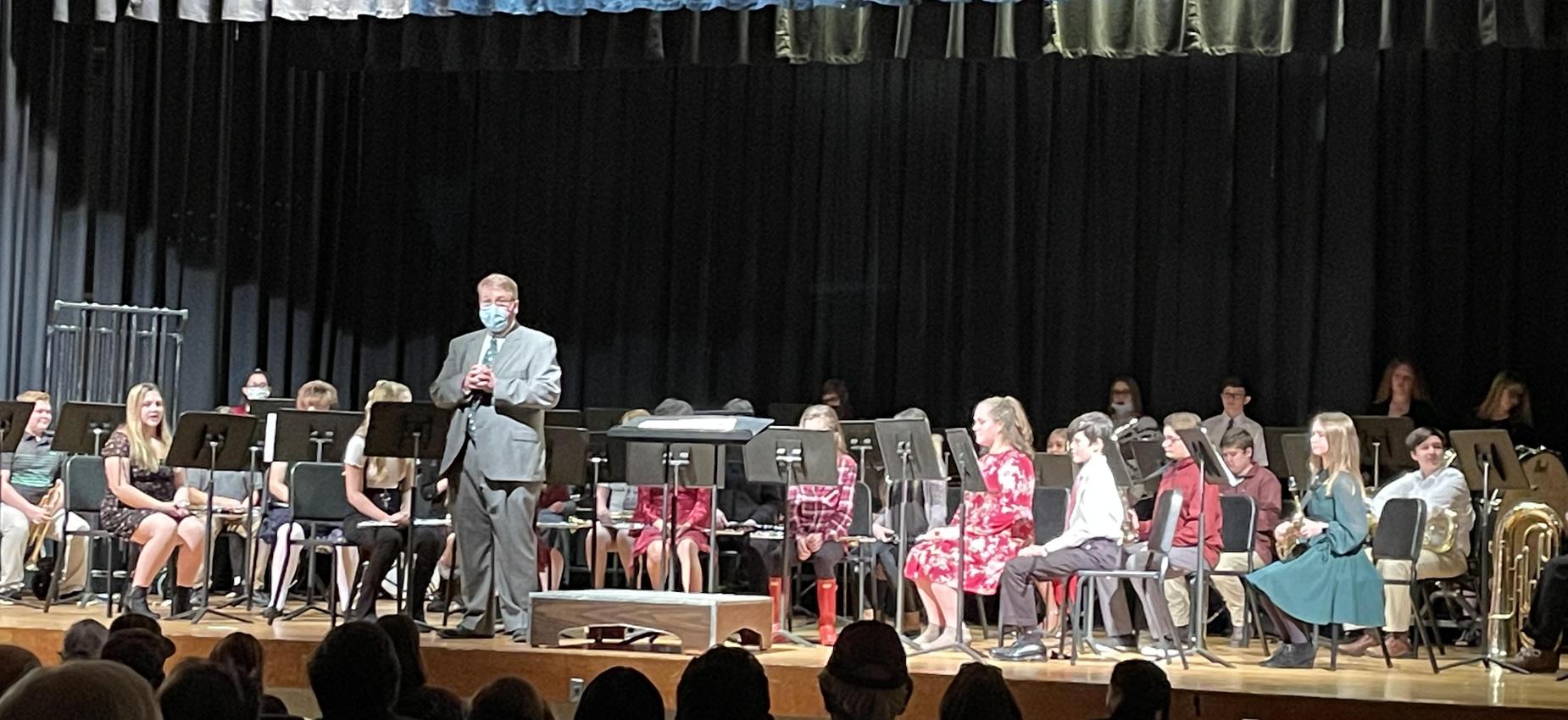 A band director stands in front of a band on a stage.