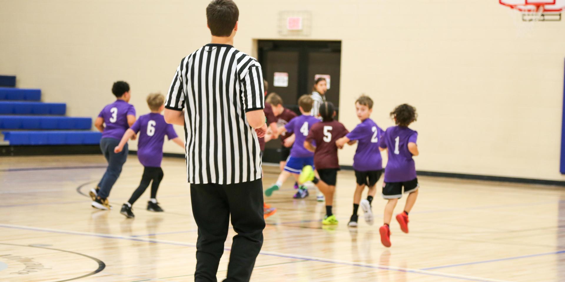 A referee watches young kids running on a basketball court.
