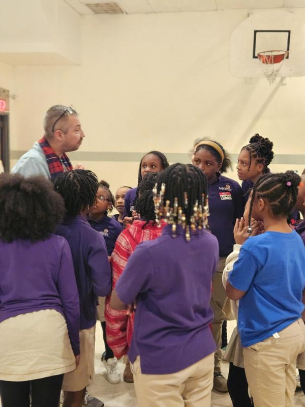 A teacher speaks to a group of scholars in a gym.