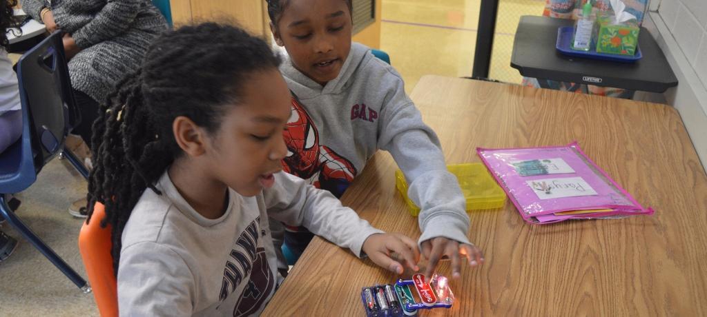 Two boys toy with a circuit to light a bulb