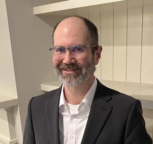 Dr. Hueslman smiling at camera wearing white shirt and dark sport coat.