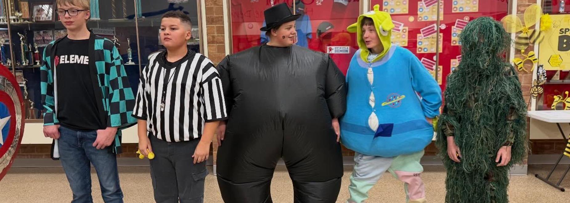 Five kids dressed in humorous or unusual costumes together in a school hallway.