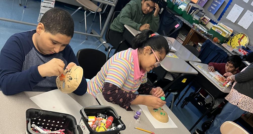 Children crafting on desks with art supplies, focusing on decorated paper and clay objects.