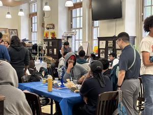 Students gather at tables, chatting and enjoying refreshments in a busy library.