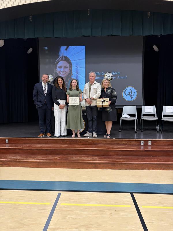 Four adults from the administration and school board pose on a stage with award winner ceci holte who is holding her award.