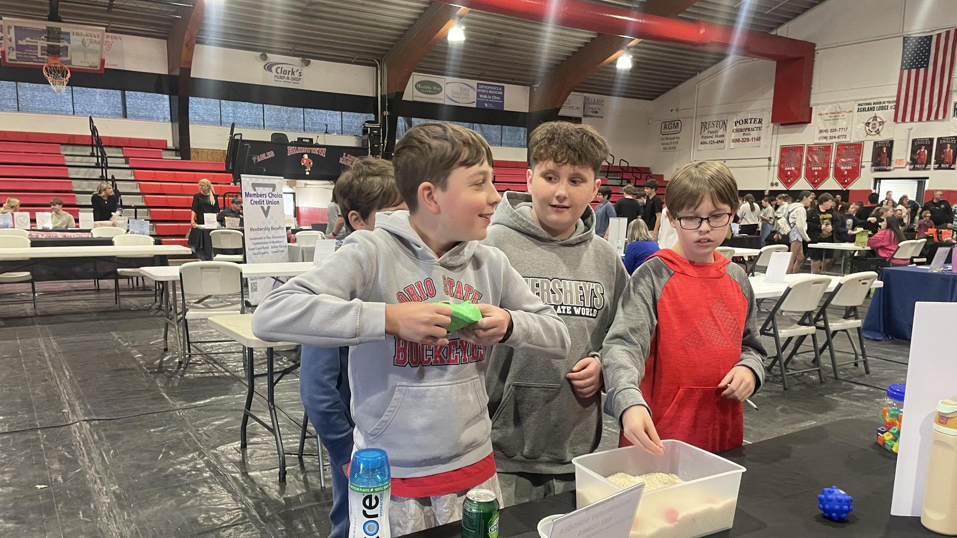 Four children interact at a table during an event in a gymnasium.