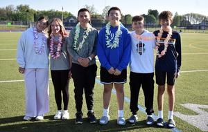 Five students in leis pose together on a sports field.