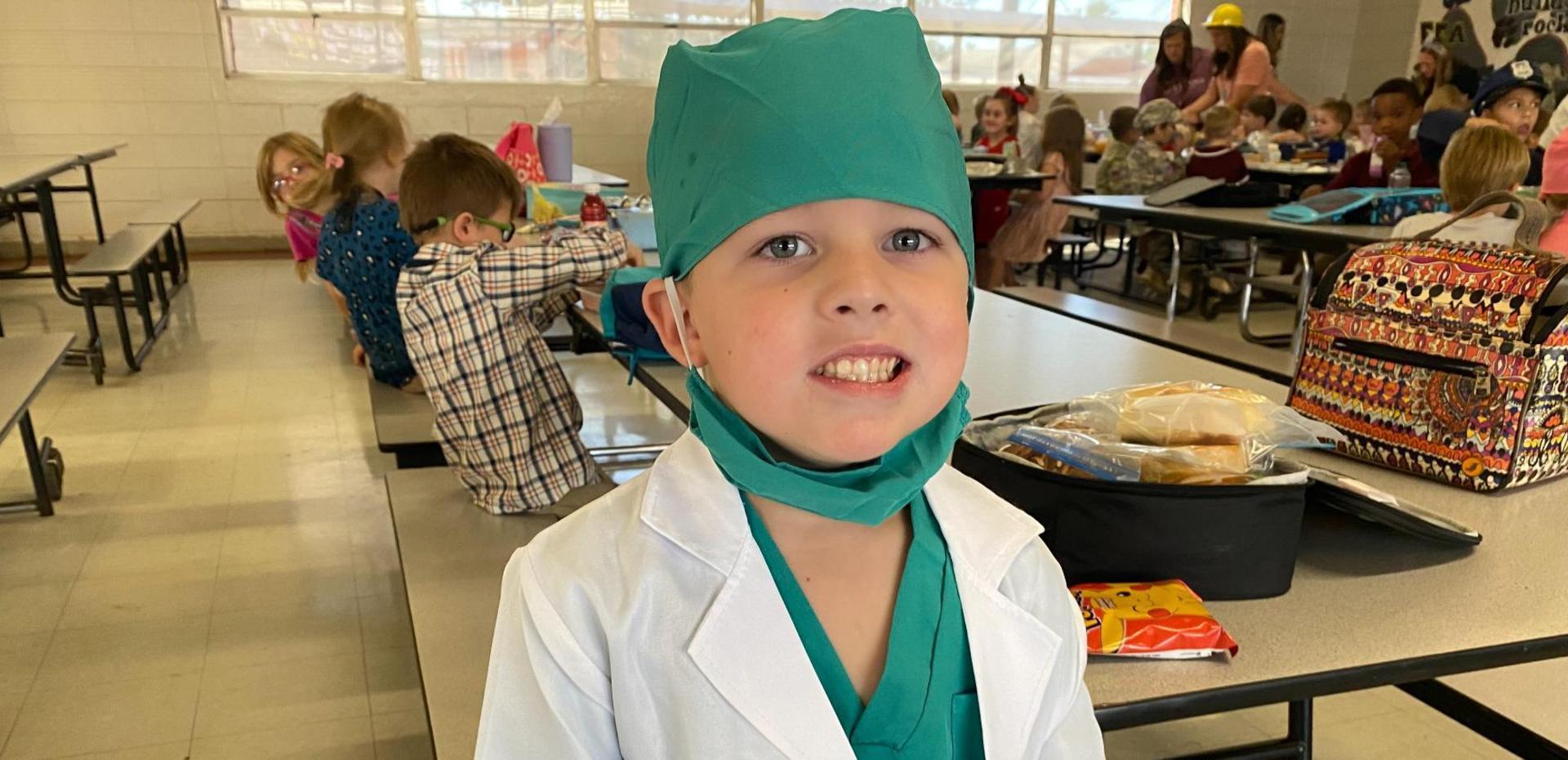 A young child in a doctor costume posing in a cafeteria.