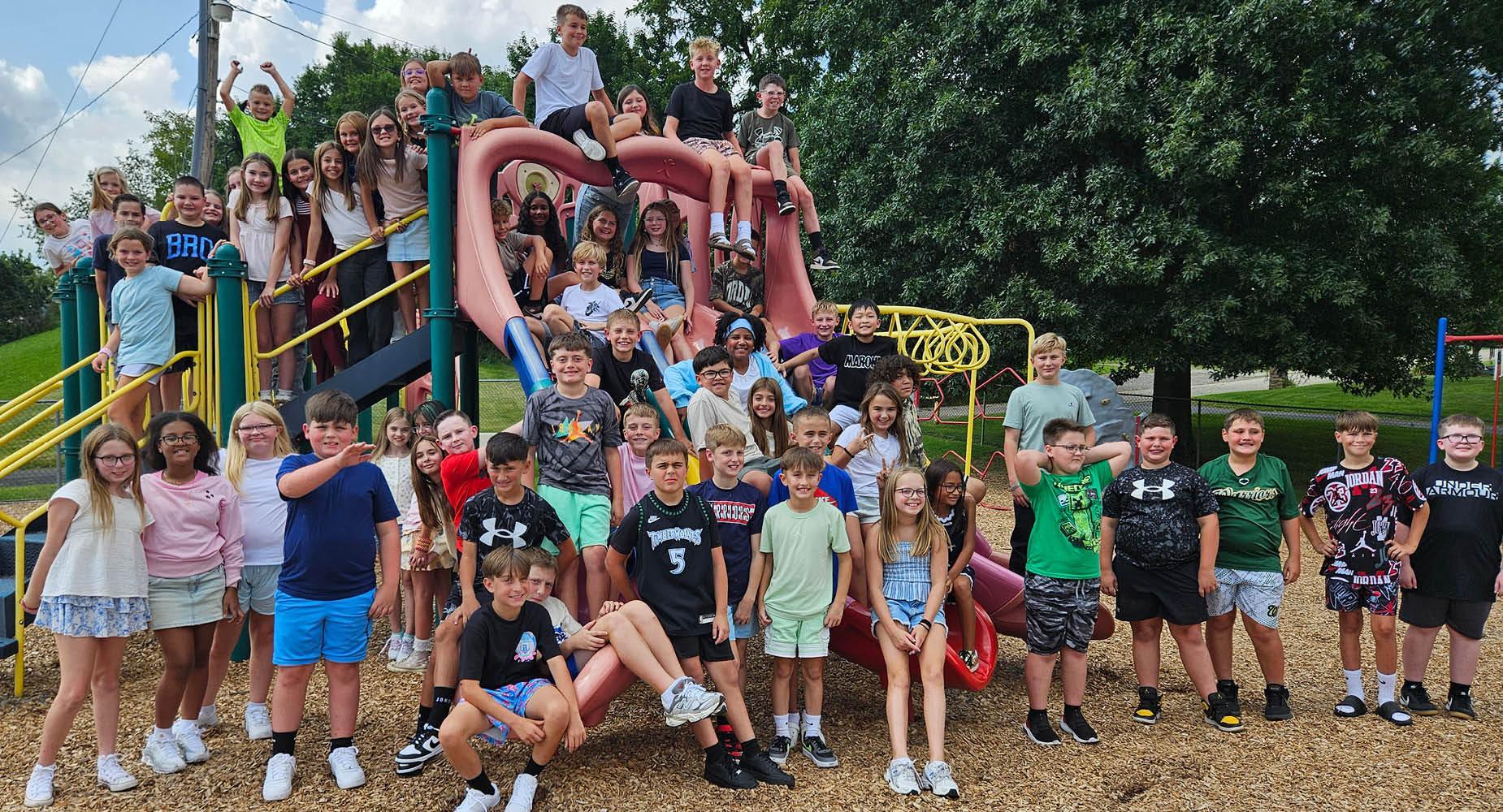 A large group of children posing joyfully on a playground slide.