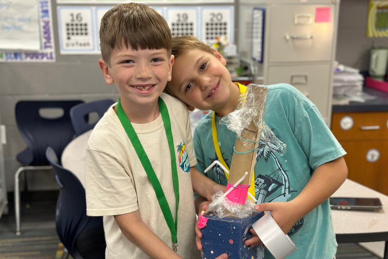 Two students holding a student-made noise maker in classroom.
