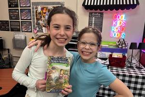 4th Graders Molly Pavlovic and Emma Dole stand together and Molly holds a book