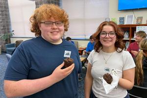 Two students smile as they hold brownies.