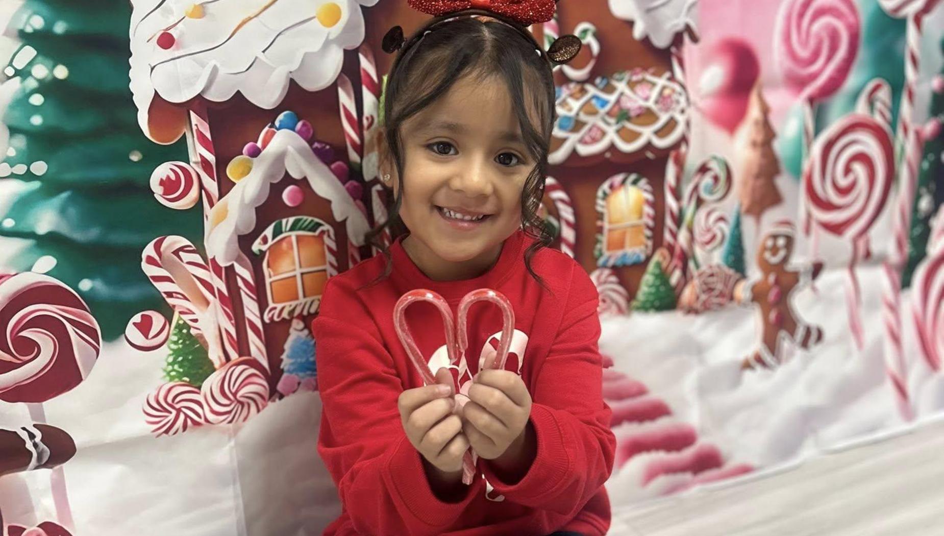 Girl holding candy canes in front of a festive background.