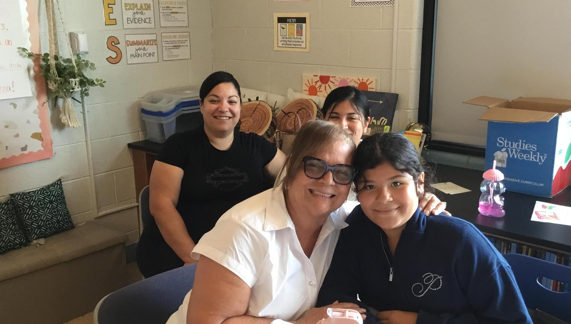 A woman with glasses and a girl smiling, with another woman in the background.