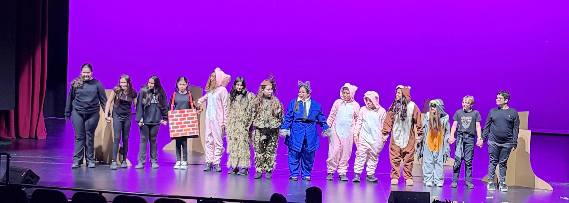 Cast members in various costumes on stage under purple lights.
