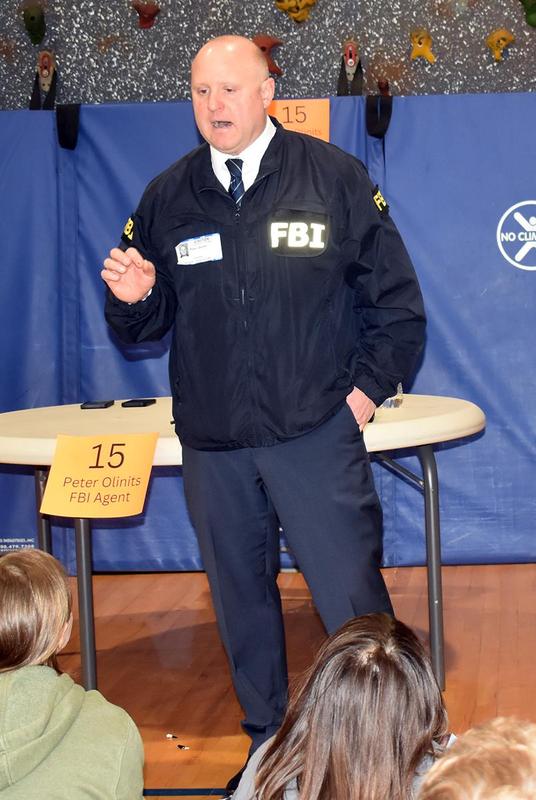 An FBI agent addresses an audience with his badge visible on his jacket.