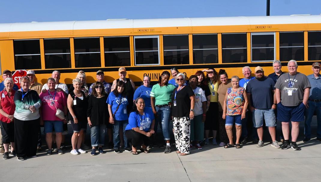 Group of people posing together in front of a yellow school bus.