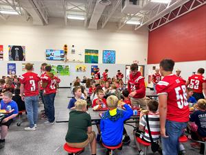 Football players eat with elementary lunch