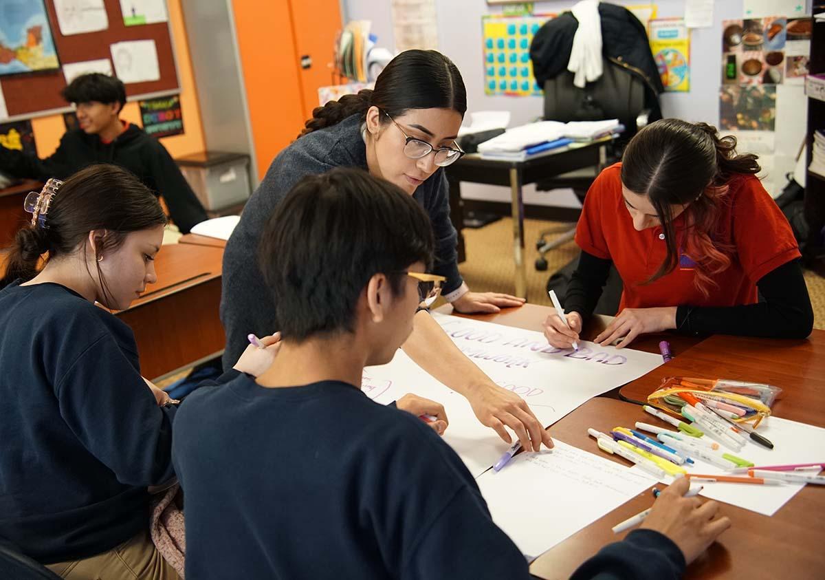 HSA Teacher smiles while kneeling beside a young student in a classroom setting.