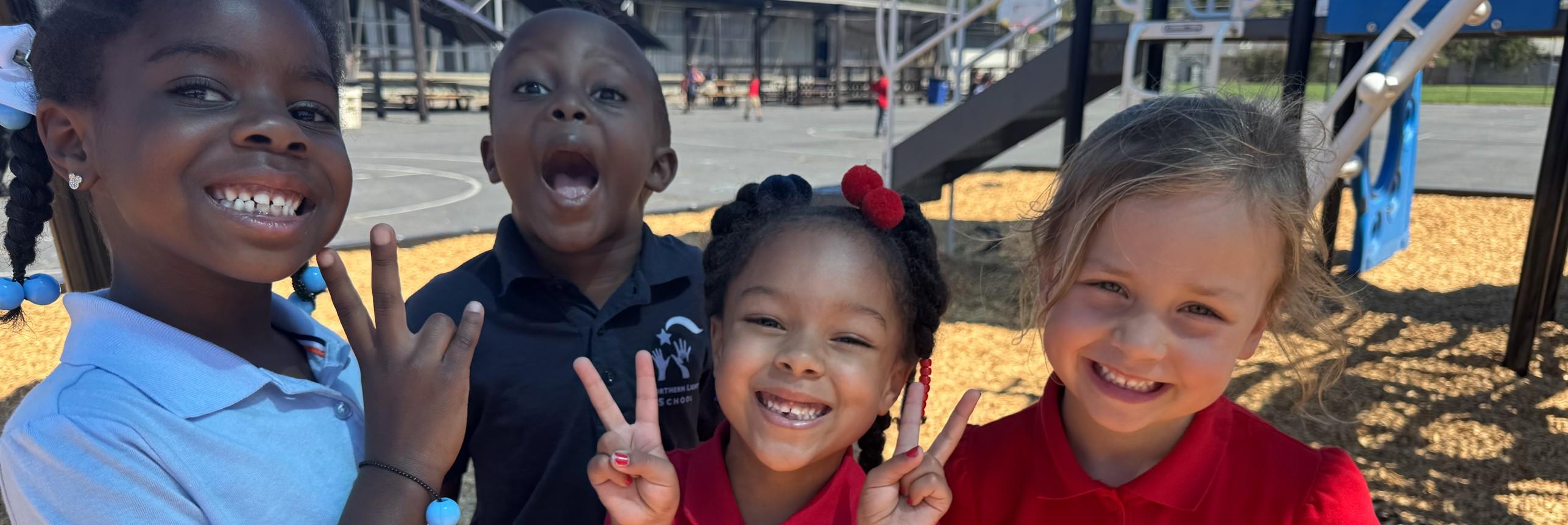 Four children smiling and making peace sign hand gestures