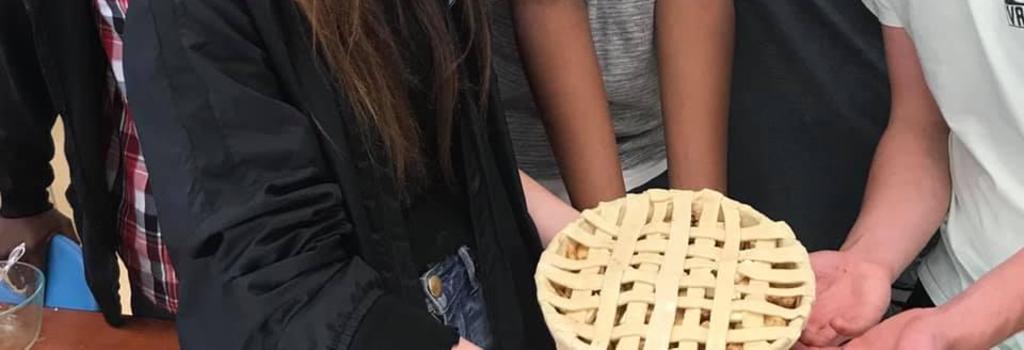 a pie prior to being backed with five students holding it