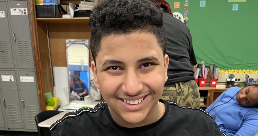 A smiling child proudly holding a handmade pumpkin figure with a hat.