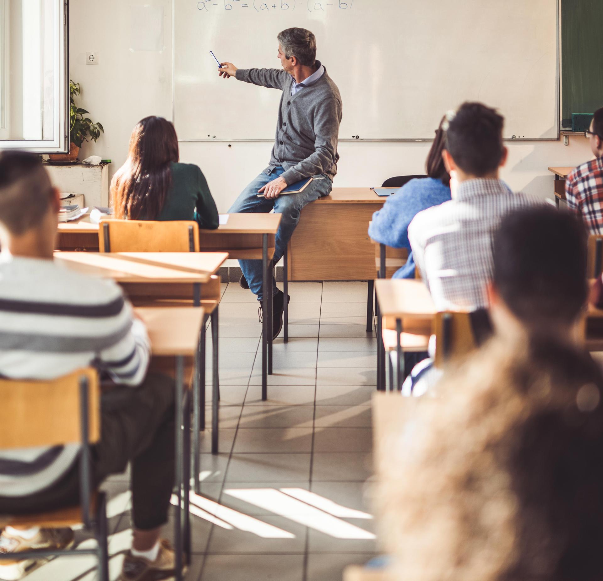 A teacher explaining a lesson to students seated in a classroom.