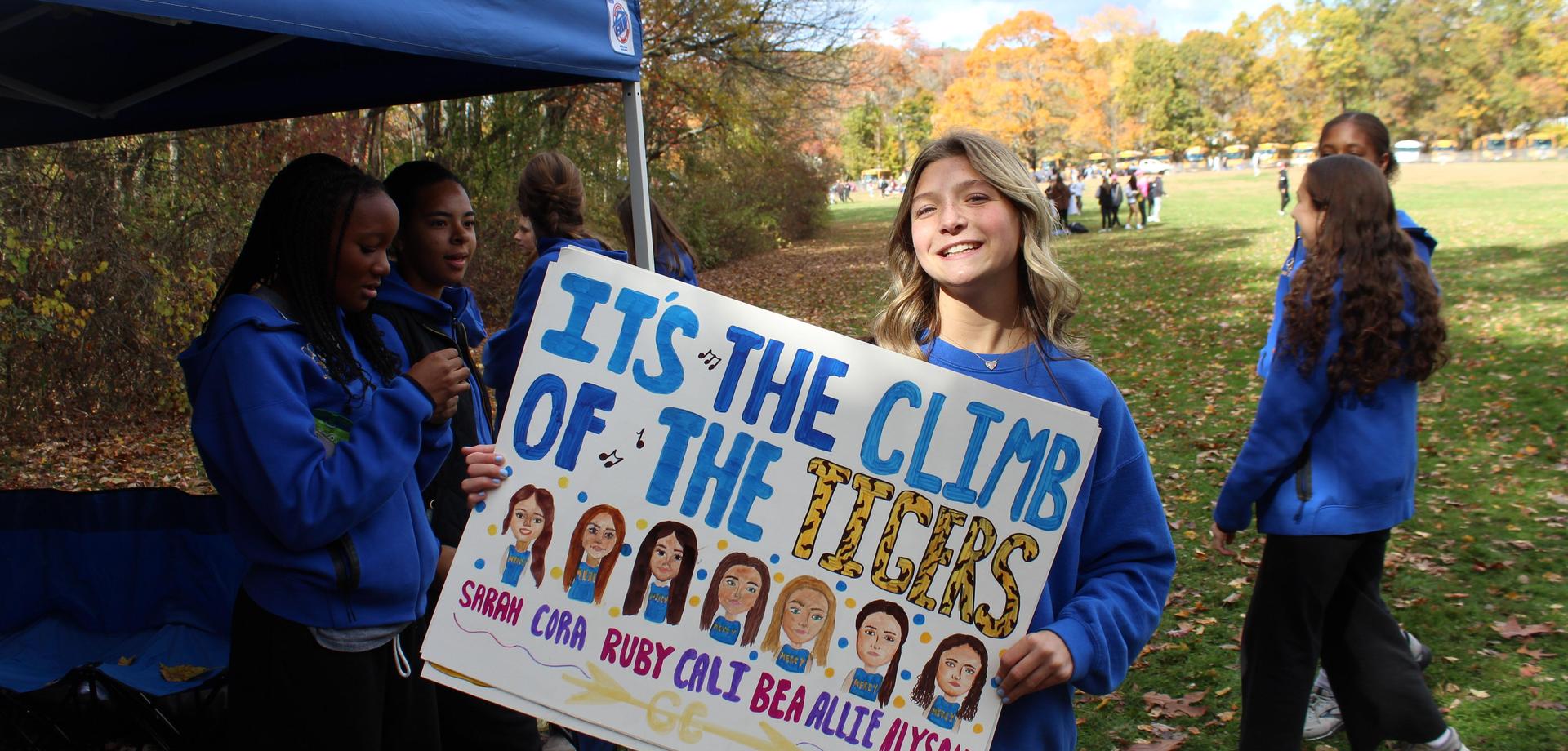 Girl holding a sign at an event with friends in the background.