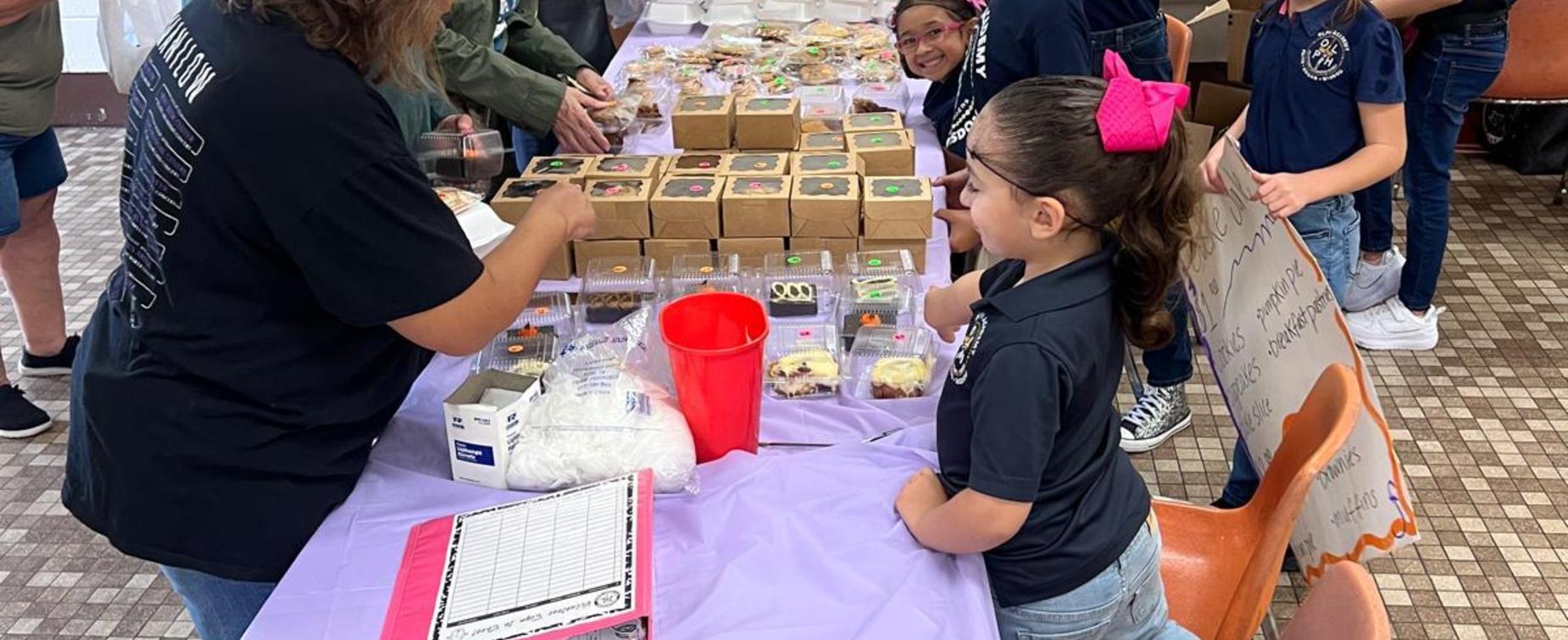 Children participating in a school bake sale with decorated treats and cookie boxes.