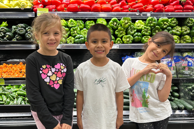 Three students standing in front of produce at United Supermarkets.