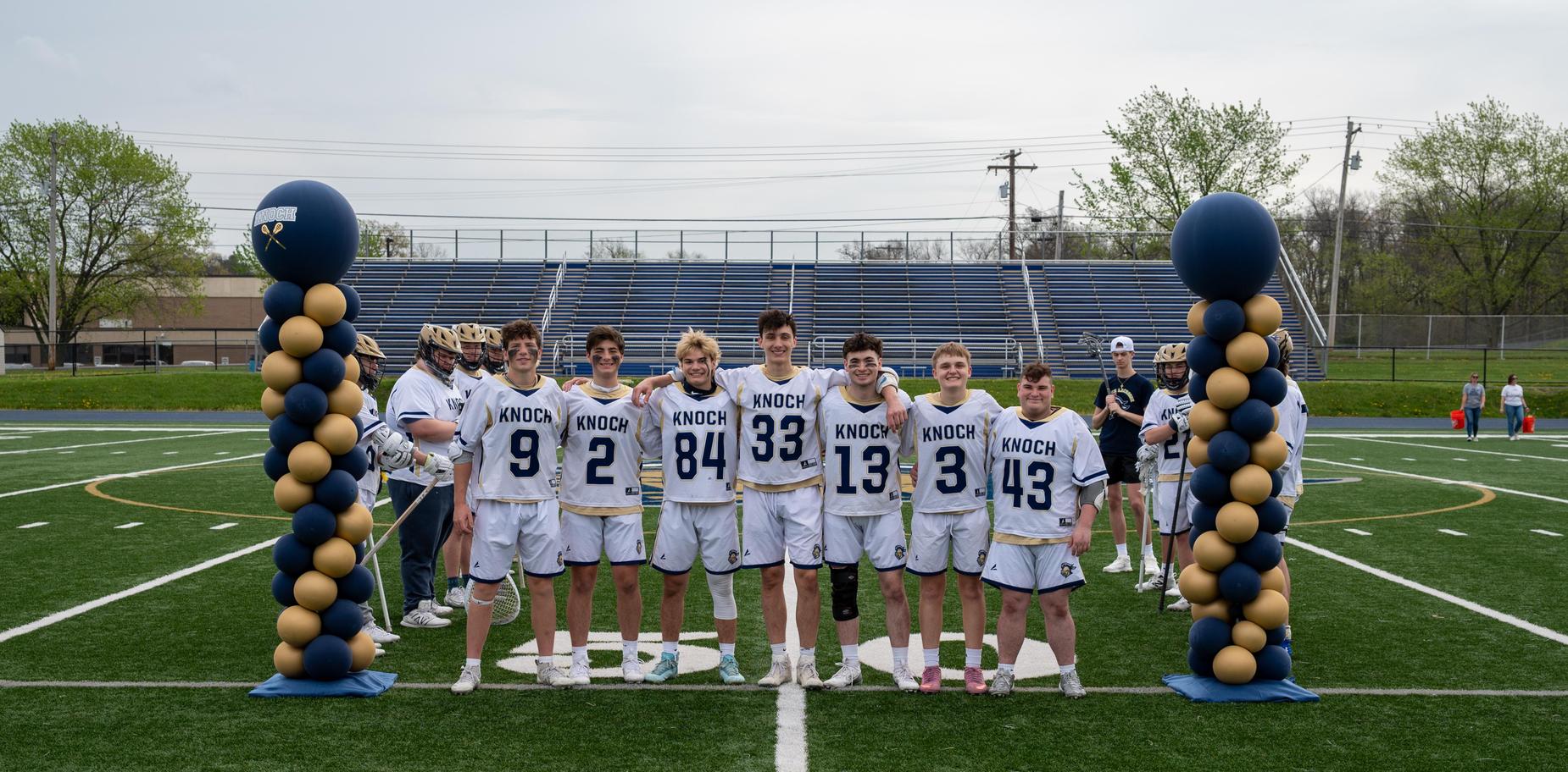 Group of ten male lacrosse players in uniforms standing before a goal.