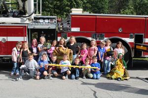 students sit beside firetruck holding equipment