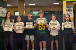 Six students holding certificates stand in a classroom