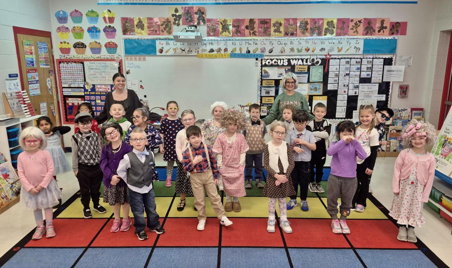 A classroom scene with students and teachers dressed in playful outfits, smiling together.