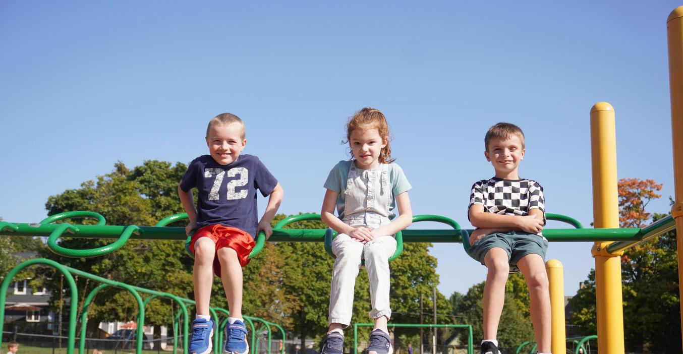 Three students sit atop a climbing bar on the playground.