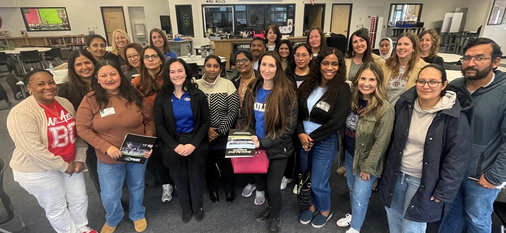 Group photo of diverse people smiling together in a classroom setting.