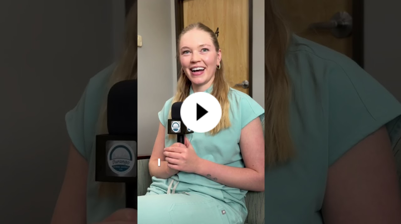 Person in light blue scrubs sitting indoors, holding a Durango School District-branded microphone and smiling during an interview.