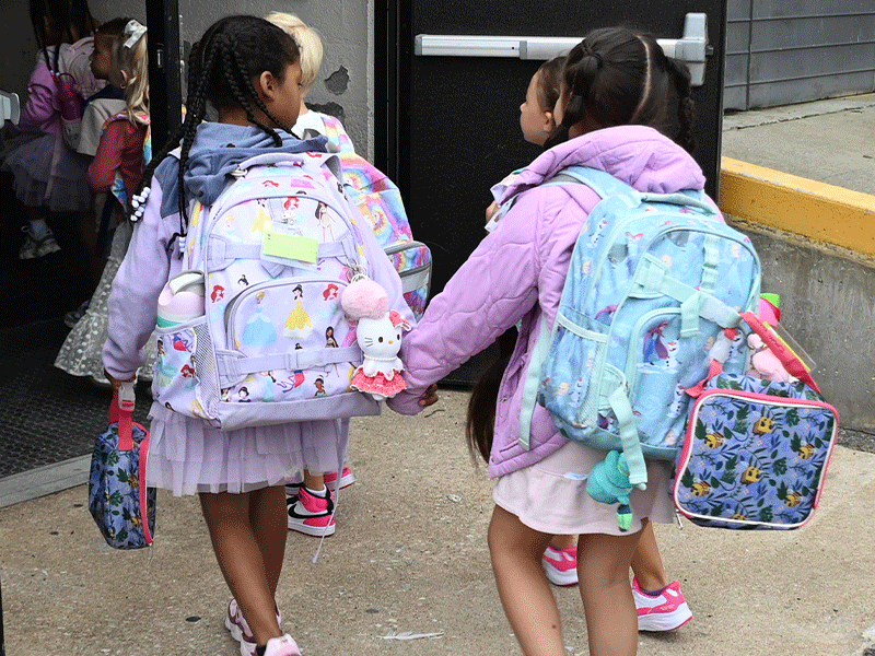 Two students with backpacks holding hands walking into school