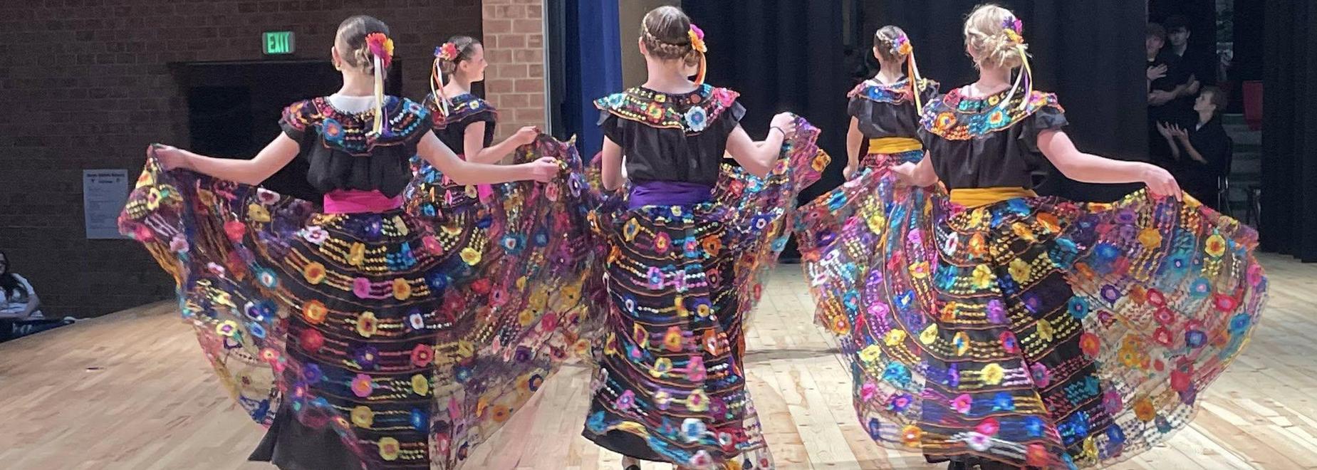 Five dancers in colorful traditional dresses performing on stage.