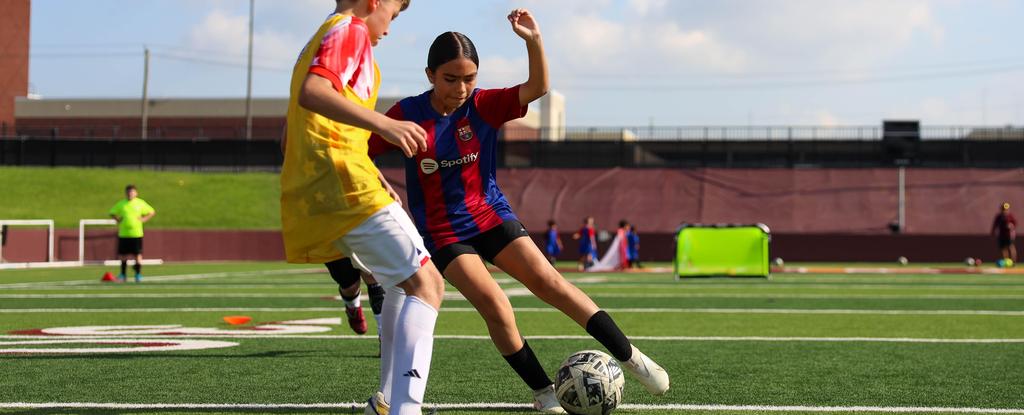 Two young soccer players competing on a field, one kicking the ball.